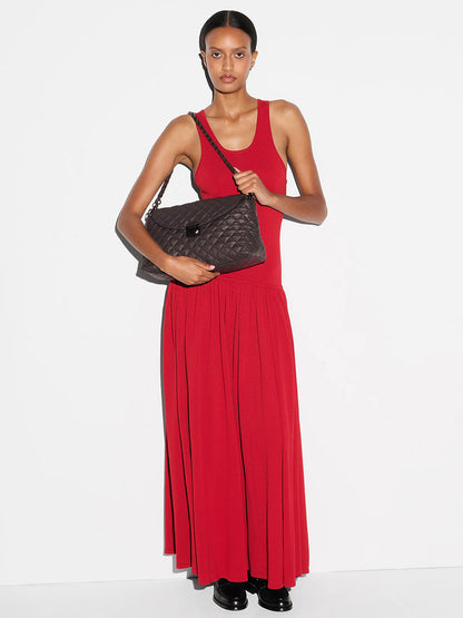 A woman in a sleeveless red maxi dress stands against a white background, holding the MZ Wallace Crosby Lock Shoulder in Espresso Oxford, paired with black shoes.