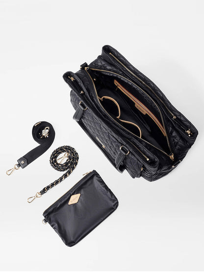 Top view of the MZ Wallace Crosby Lock Tote in Black Oxford quilted designer work bag with gold zippers, showing an open interior. Accessories include a black strap, a braided strap, and a small matching pouch, all placed neatly beside the elegant tote.