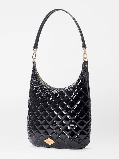 The MZ Wallace Crosby Sienna in Black Lacquer Oxford features glossy quilted black fabric, a single shoulder strap, gold-tone hardware, a gold logo plaque on the front, and refined Italian leather trim.