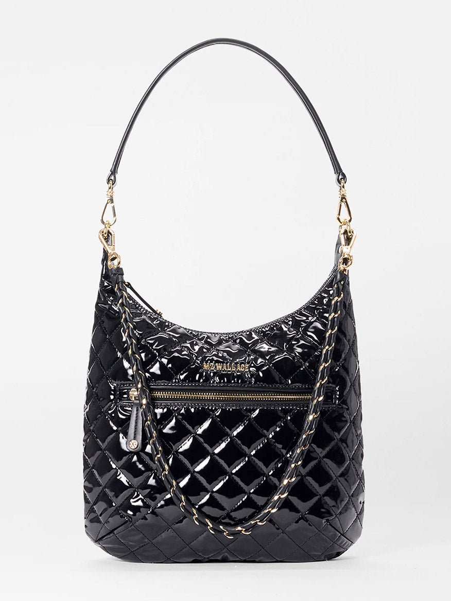 The MZ Wallace Crosby Sienna in Black Lacquer Oxford features glossy quilted black oxford, a top handle, gold-tone hardware, Italian leather trim, front zipper pocket, and an attached chain strap, shown on a plain white background.