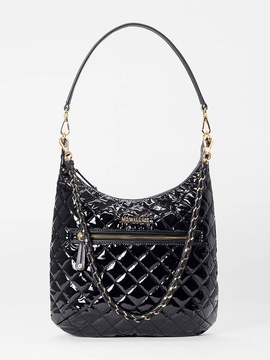 The MZ Wallace Crosby Sienna in Black Lacquer Oxford features glossy quilted black oxford, a top handle, gold-tone hardware, Italian leather trim, front zipper pocket, and an attached chain strap, shown on a plain white background.