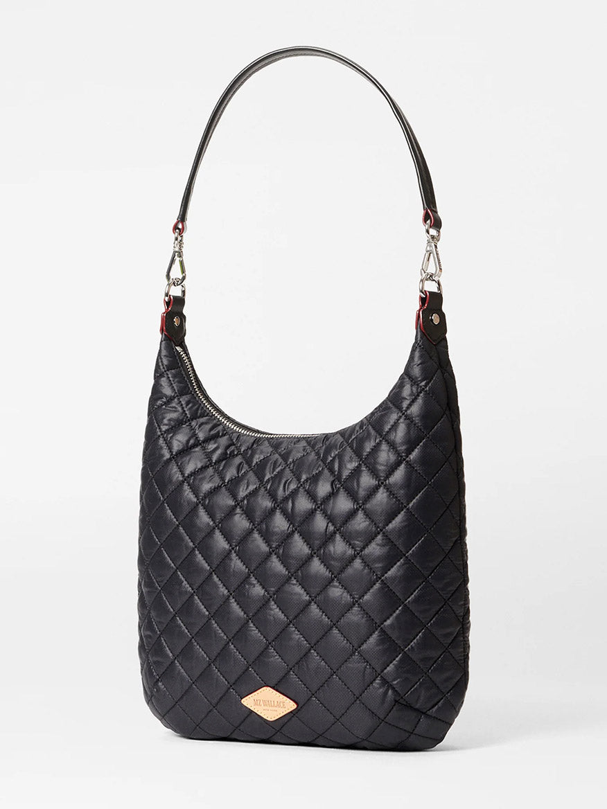 The MZ Wallace Crosby Sienna in Black Oxford is a black quilted handbag with a detachable chain strap, crafted from fine Italian leather. It boasts a diamond pattern and a small logo patch near the base, blending elegance with versatility.