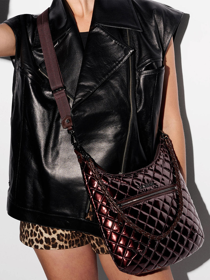 Person wearing a sleeveless black leather jacket and leopard print skirt, carrying the MZ Wallace Crosby Sienna in Bordeaux Lacquer Oxford with a wide strap.