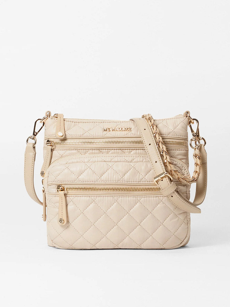 The MZ Wallace Downtown Crosby in Buff Oxford is a beige quilted crossbody bag made from Italian leather, accented with gold zippers and a chain-adjustable strap, set against a white background.