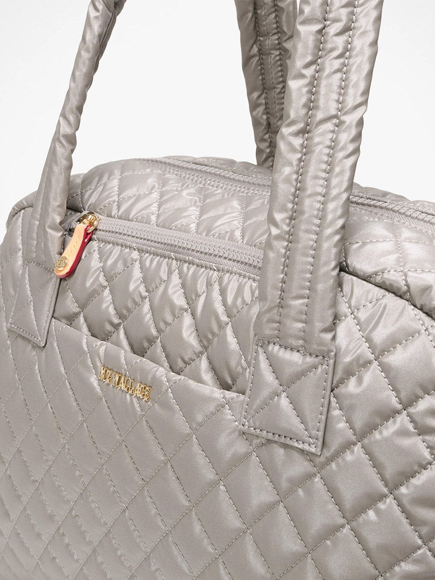 Close-up of the MZ Wallace Jimmy Deluxe in Sable Pearl Metallic, a quilted silver-gray laptop bag with padded handles, Italian leather trim, top zipper, gold brand lettering, and a detachable strap for versatility.