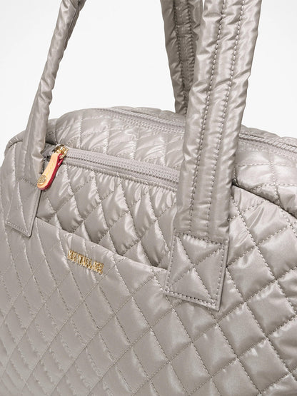 Close-up of the MZ Wallace Jimmy Deluxe in Sable Pearl Metallic, a quilted silver-gray laptop bag with padded handles, Italian leather trim, top zipper, gold brand lettering, and a detachable strap for versatility.