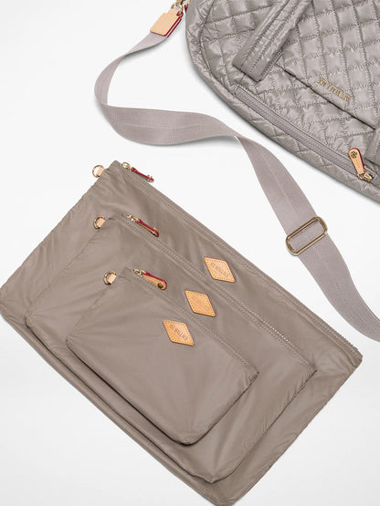 Three taupe zippered pouches in various sizes sit beside the MZ Wallace Jimmy Deluxe in Sable Pearl Metallic, a quilted laptop bag with an adjustable strap and gold hardware, all displayed on a white surface.