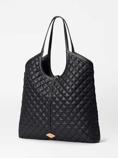 The MZ Wallace Large Astor Tote in Black Oxford features quilted fabric, Italian leather handles, and a small tan label on the lower front, shown against a plain white background.