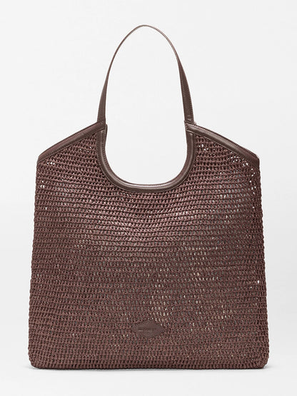 The MZ Wallace Large Crochet Georgica Tote features brown crochet, two handles, gold hardware, and Italian leather trim at the top, displayed against a plain light background.