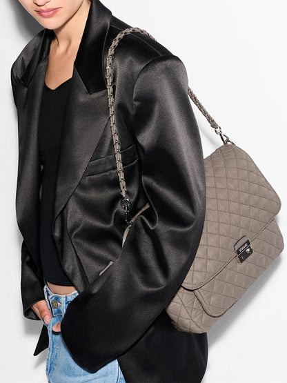 Person wearing a black satin blazer and blue jeans, carrying the MZ Wallace Crosby Lock Large Crossbody in Morning Dove Oxford—a quilted designer bag with a chic chain strap.