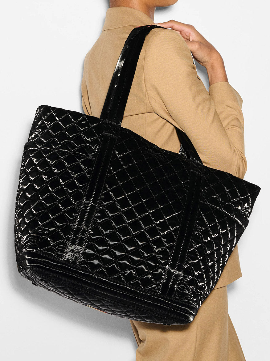 A person is holding an MZ Wallace Large Empire Tote in Black Liquid Oxford and wearing a tan blazer, showcasing an effortlessly stylish lightweight bag that complements their ensemble.