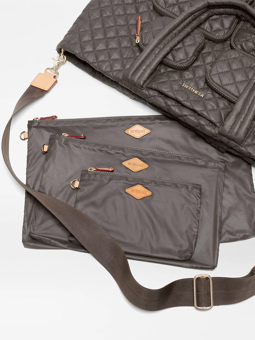 The MZ Wallace Large Metro Travel Tote in Magnet Oxford features quilted gray nylon, an adjustable shoulder strap, and three matching zippered pouches of different sizes, all displayed on a white surface.