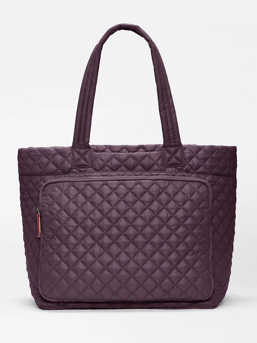 The MZ Wallace Large Metro Travel Tote in Raisin Oxford features a quilted diamond pattern design in a rich purple shade, two sturdy handles, and a front zippered pocket for organized storage. Made from recycled nylon, this tote is shown against a plain white background.