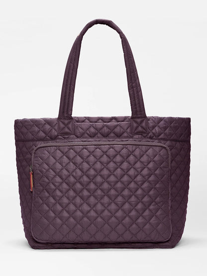 The MZ Wallace Large Metro Travel Tote in Raisin Oxford features a quilted diamond pattern design in a rich purple shade, two sturdy handles, and a front zippered pocket for organized storage. Made from recycled nylon, this tote is shown against a plain white background.