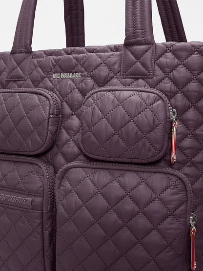 Close-up of the MZ Wallace Large Metro Travel Tote in Raisin Oxford, showcasing its quilted design crafted from recycled nylon, multiple zippered pockets for organized storage, and signature “MZ WALLACE” branding on the front.