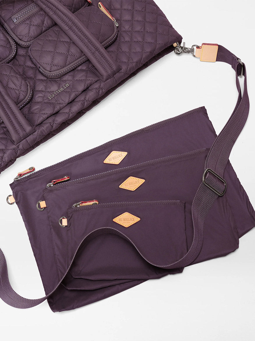 The MZ Wallace Large Metro Travel Tote in Raisin Oxford, crafted from quilted recycled nylon in a rich purple hue and featuring tan leather accents, includes three coordinated zippered pouches attached to an adjustable shoulder strap for organized carry.