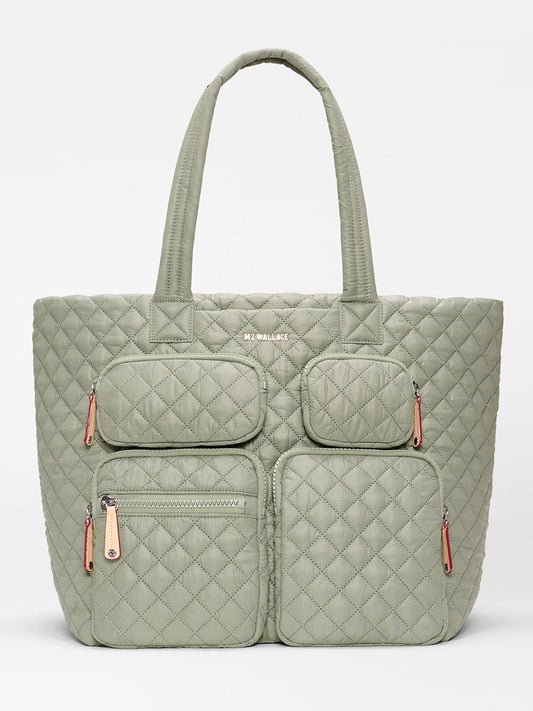 The MZ Wallace Large Metro Travel Tote in Agave Green Oxford features two top handles, four front zippered pockets, a visible brand name near the top center, and a nylon crossbody strap for versatile carrying.