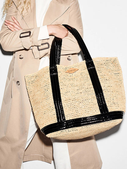 A woman in a trench coat holding a MZ Wallace Large Raffia Tote in Raffia/Black.