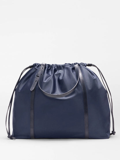 The MZ Wallace Large Waverly Tote in Dawn Bedford is a spacious navy tote with thin black Italian leather straps, a minimalist design, and fits a 15" laptop.