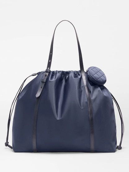 The MZ Wallace Large Waverly Tote in Dawn Bedford features black Italian leather straps, a small quilted round pouch near the top, and a spacious navy blue interior that fits a 15" laptop.