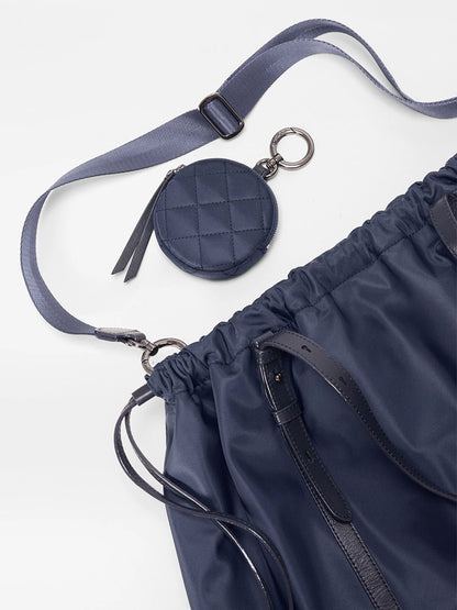 The MZ Wallace Large Waverly Tote in Dawn Bedford is a navy blue bag with Italian leather straps, a detachable quilted coin pouch, adjustable crossbody strap, and space for a 15" laptop, shown on a white background.