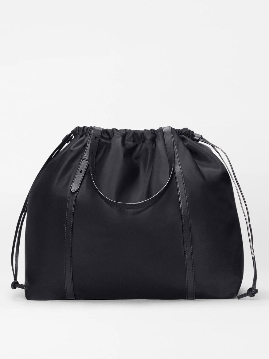 The MZ Wallace Large Waverly Tote in Black Bedford is a spacious black tote with leather accents, Italian leather handles, and a circular handle, designed to fit a 15" laptop. Shown against a plain white background.