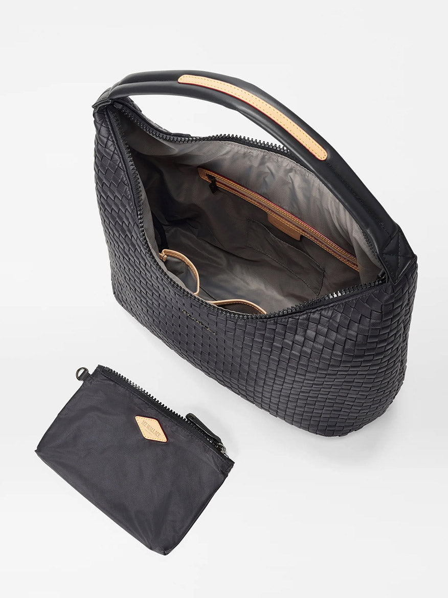 The MZ Wallace Large Woven Shoulder Bag in Black Oxford features a black woven nylon exterior with an open zipper revealing internal compartments, perfect for daily organization. Inside, you'll find enough space to include a pair of glasses and more. A smaller black zippered pouch accompanies this lightweight shoulder bag.