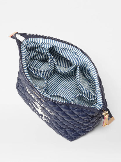 The MZ Wallace Large Zoey Cosmetic in Anchor Oxford is a navy quilted pouch with a zippered top, blue and white striped interior, and multiple compartments—perfect for organizing essentials when traveling.