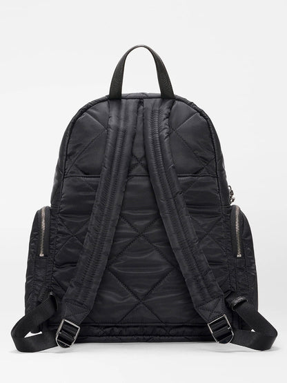 The MZ Wallace Madison Backpack in Black Bedford features quilted design, two padded adjustable shoulder straps, a top handle, zippered side pockets, and a luggage sleeve, shown against a plain light background.