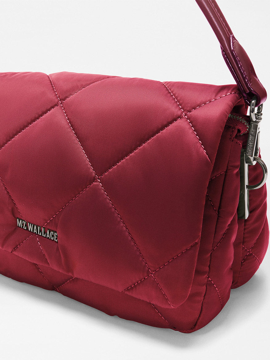 Close-up of the MZ Wallace Madison Flap Crossbody in Claret Bedford, a quilted red handbag made from recycled Bedford nylon, featuring a shiny strap, metal zipper, and “MZ WALLACE” logo on the side.