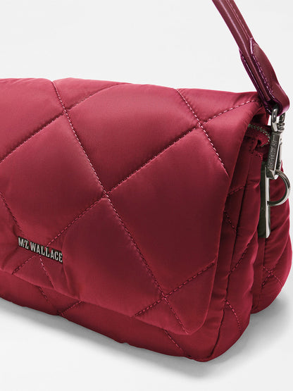 Close-up of the MZ Wallace Madison Flap Crossbody in Claret Bedford, a quilted red handbag made from recycled Bedford nylon, featuring a shiny strap, metal zipper, and “MZ WALLACE” logo on the side.