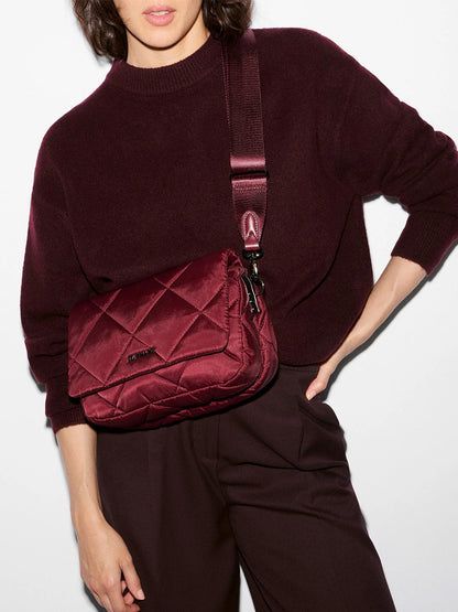 A woman poses in a dark burgundy sweater and trousers, styled with the MZ Wallace Madison Flap Crossbody in Claret Bedford—a chic quilted crossbody bag crafted from recycled Bedford nylon—set against a plain light background.