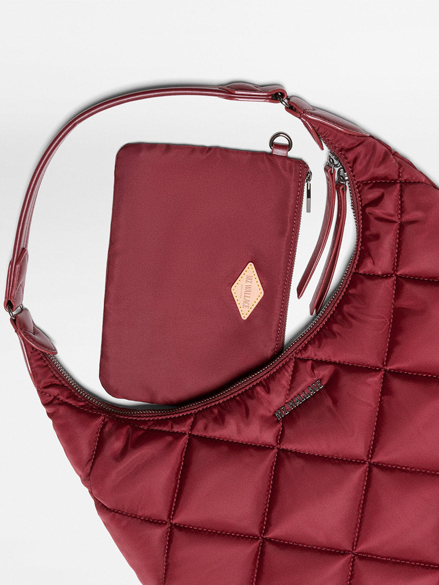 The MZ Wallace Madison Shoulder in Claret Bedford, crafted from luxurious Italian leather in a quilted maroon finish, is displayed on a white background with a matching zippered pouch placed inside.