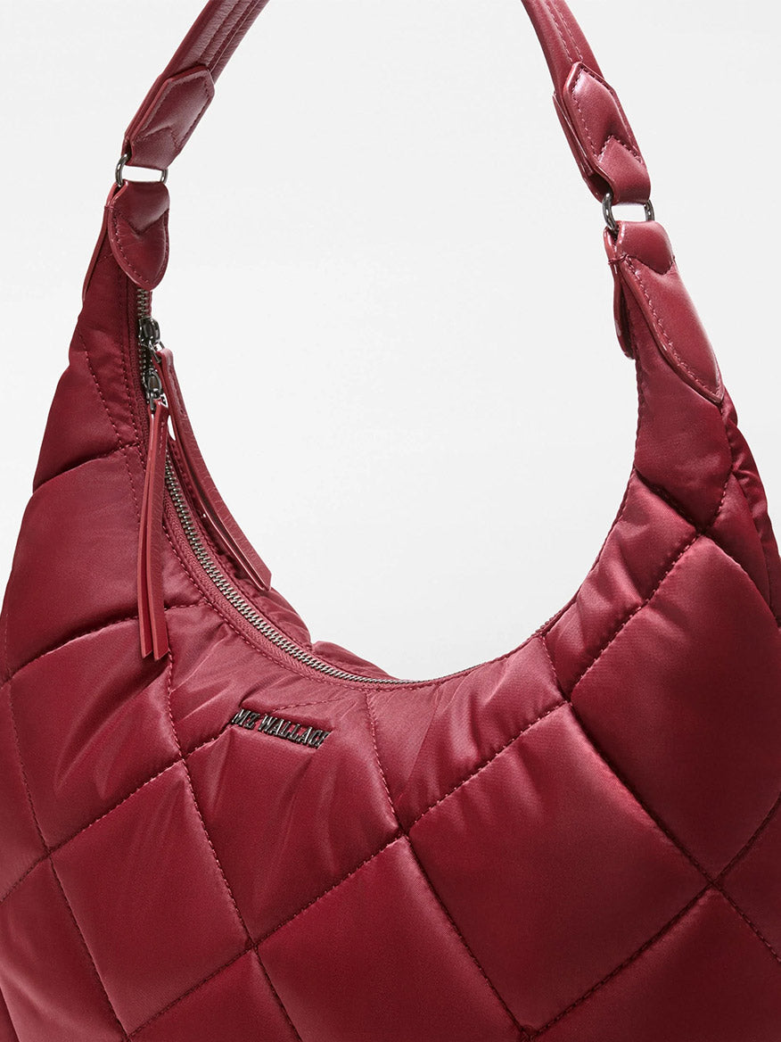Close-up of the MZ Wallace Madison Shoulder in Claret Bedford, a red quilted shoulder bag crafted from luxurious Italian leather, featuring a curved handle, zipper closure, and a small metallic brand label on the front.