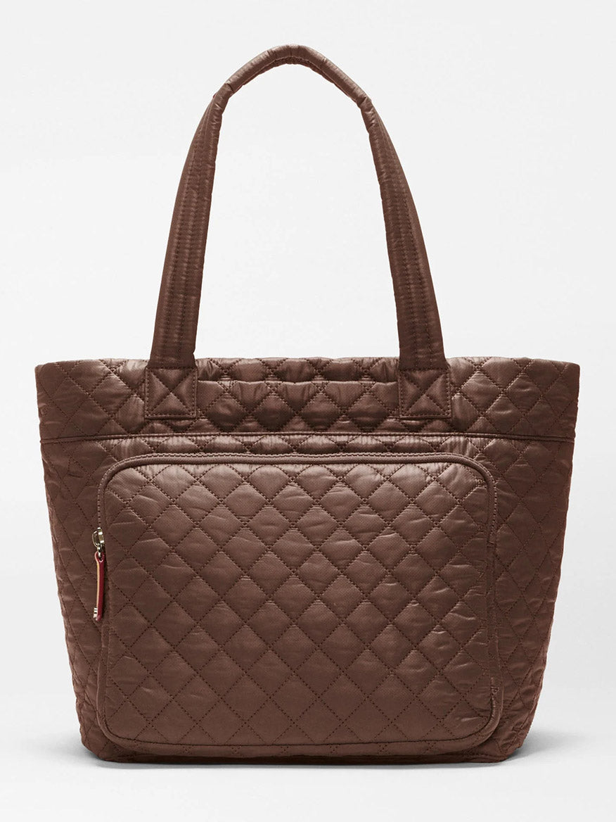 The MZ Wallace Medium Metro Travel Tote in Walnut Oxford is a quilted brown commuter bag featuring two handles and a spacious front zippered pocket, crafted from recycled nylon and shown against a plain white background.