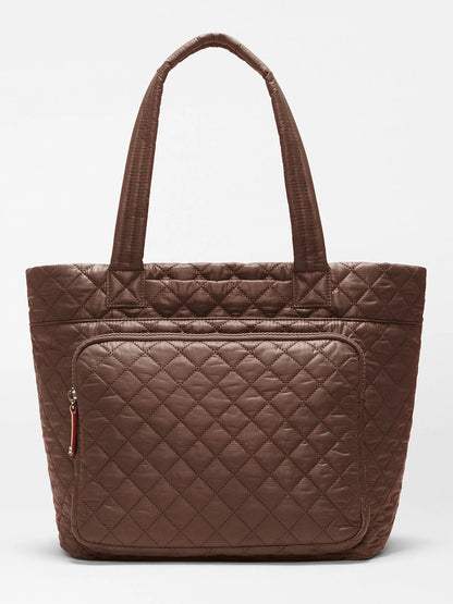 The MZ Wallace Medium Metro Travel Tote in Walnut Oxford is a quilted brown commuter bag featuring two handles and a spacious front zippered pocket, crafted from recycled nylon and shown against a plain white background.