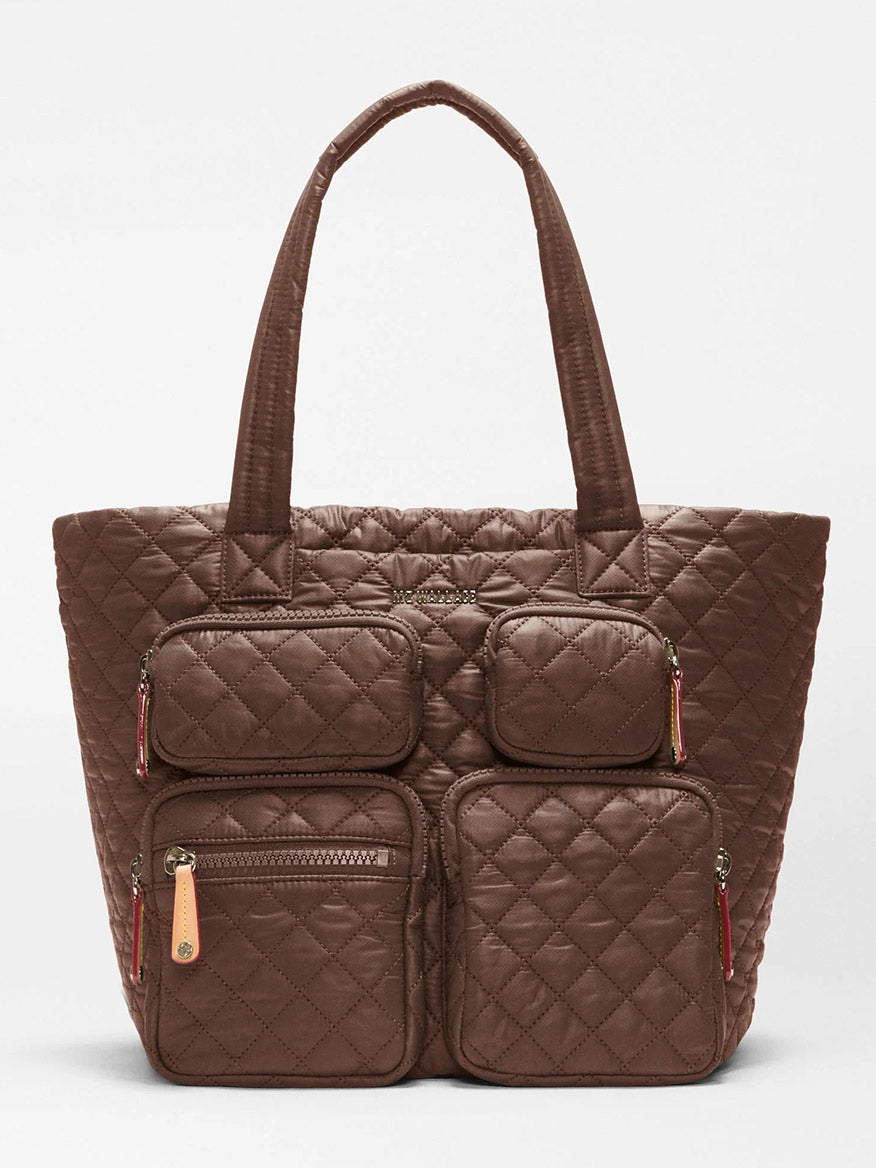 The MZ Wallace Medium Metro Travel Tote in Walnut Oxford is a brown quilted tote bag made from durable recycled nylon, featuring diamond-shaped stitching on the exterior, four front zippered pockets, and two shorter handles—making it a stylish and eco-friendly choice for commuters.