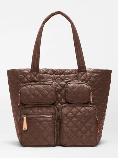 The MZ Wallace Medium Metro Travel Tote in Walnut Oxford is a brown quilted tote bag made from durable recycled nylon, featuring diamond-shaped stitching on the exterior, four front zippered pockets, and two shorter handles—making it a stylish and eco-friendly choice for commuters.
