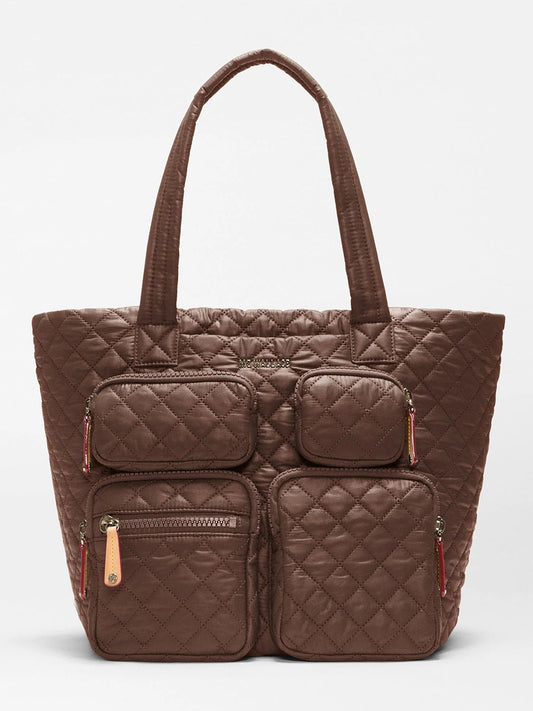The MZ Wallace Medium Metro Travel Tote in Walnut Oxford is a brown quilted tote bag made from durable recycled nylon, featuring diamond-shaped stitching on the exterior, four front zippered pockets, and two shorter handles—making it a stylish and eco-friendly choice for commuters.