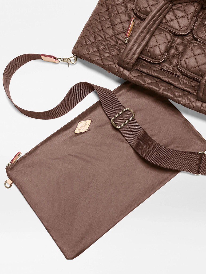 The MZ Wallace Medium Metro Travel Tote in Walnut Oxford is partially shown on a white surface, with its detachable flat brown pouch and adjustable strap laid out alongside it.