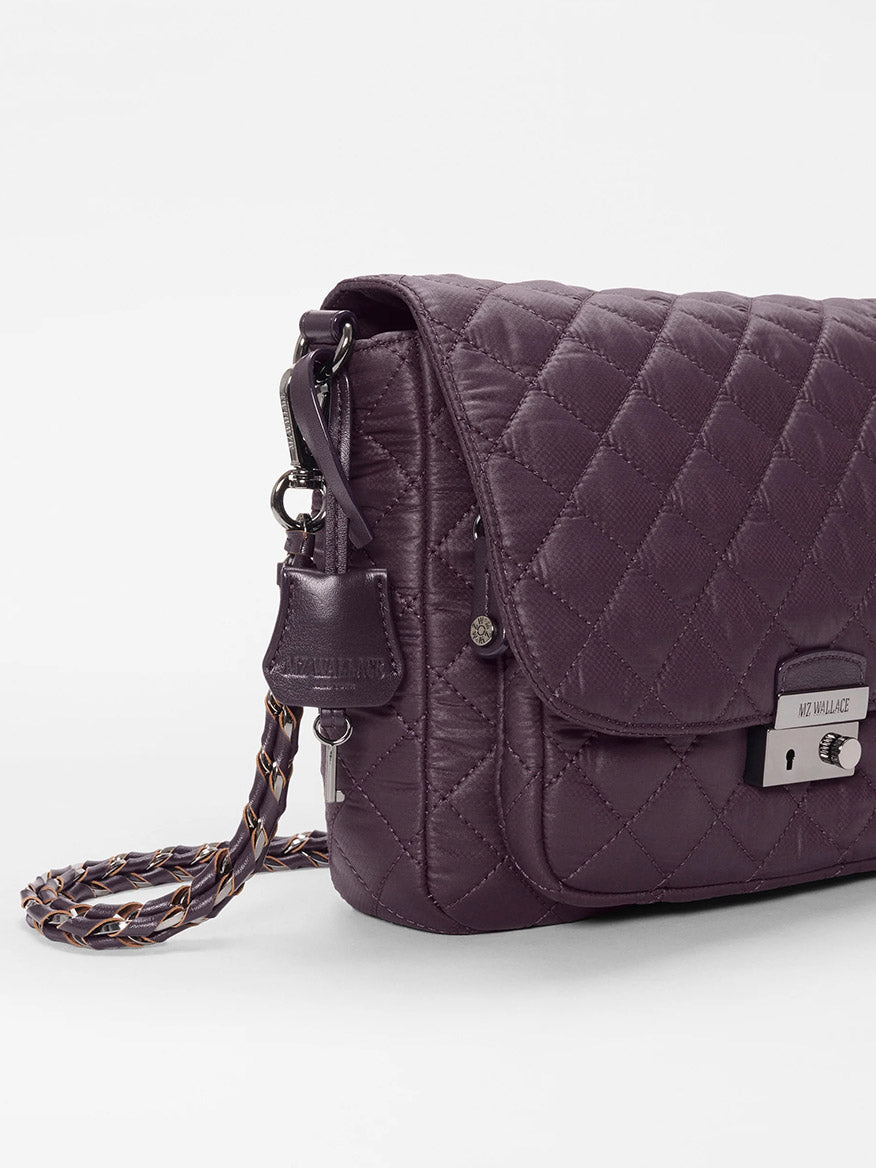 The MZ Wallace Crosby Lock Medium Crossbody in Raisin Oxford is a quilted dark purple crossbody bag with a braided strap, metal clasp, and a small logo tag on the side. It features stylish Italian leather trim and is shown against a plain white background.