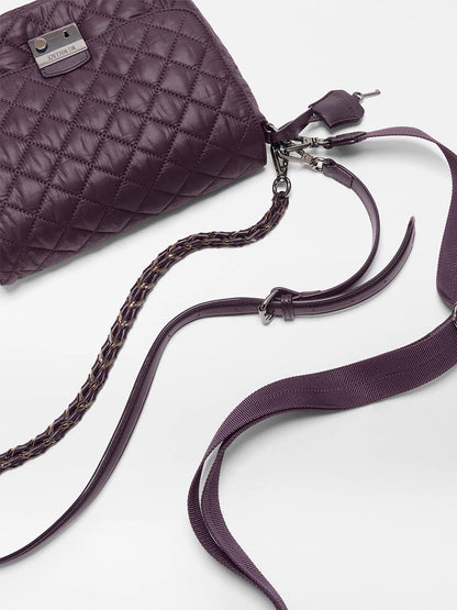 The MZ Wallace Crosby Lock Medium Crossbody in Raisin Oxford is a quilted purple recycled nylon handbag with Italian leather trim, featuring a metal logo plate, braided strap detail, and a detachable shoulder strap, displayed on a white surface.