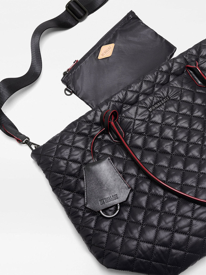 MZ Wallace Medium Daily Tote in Black Oxford, featuring quilted recycled nylon, an adjustable shoulder strap, red accents, an attached leather tag, and a matching zippered pouch, displayed on a white background.