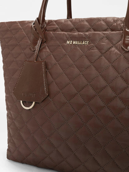 Close-up of the MZ Wallace Medium Daily Tote in Walnut Oxford, featuring brown quilted recycled nylon, “MZ WALLACE” gold lettering, and a matching leather tag attached to one handle.