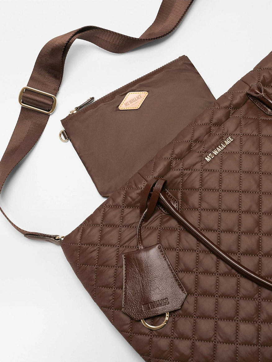 The MZ Wallace Medium Daily Tote in Walnut Oxford—a stylish brown quilted bag made from recycled nylon—serves as a fashionable laptop tote, complete with a matching detachable pouch, adjustable shoulder strap, and leather tag, all beautifully displayed on a white surface.