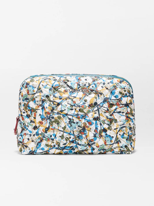 The MZ Wallace Medium Double Zip Cosmetic in Club Paint Oxford is a rectangular quilted pouch with zippers, featuring an abstract splatter paint pattern in blue, green, yellow, and orange on a white background.