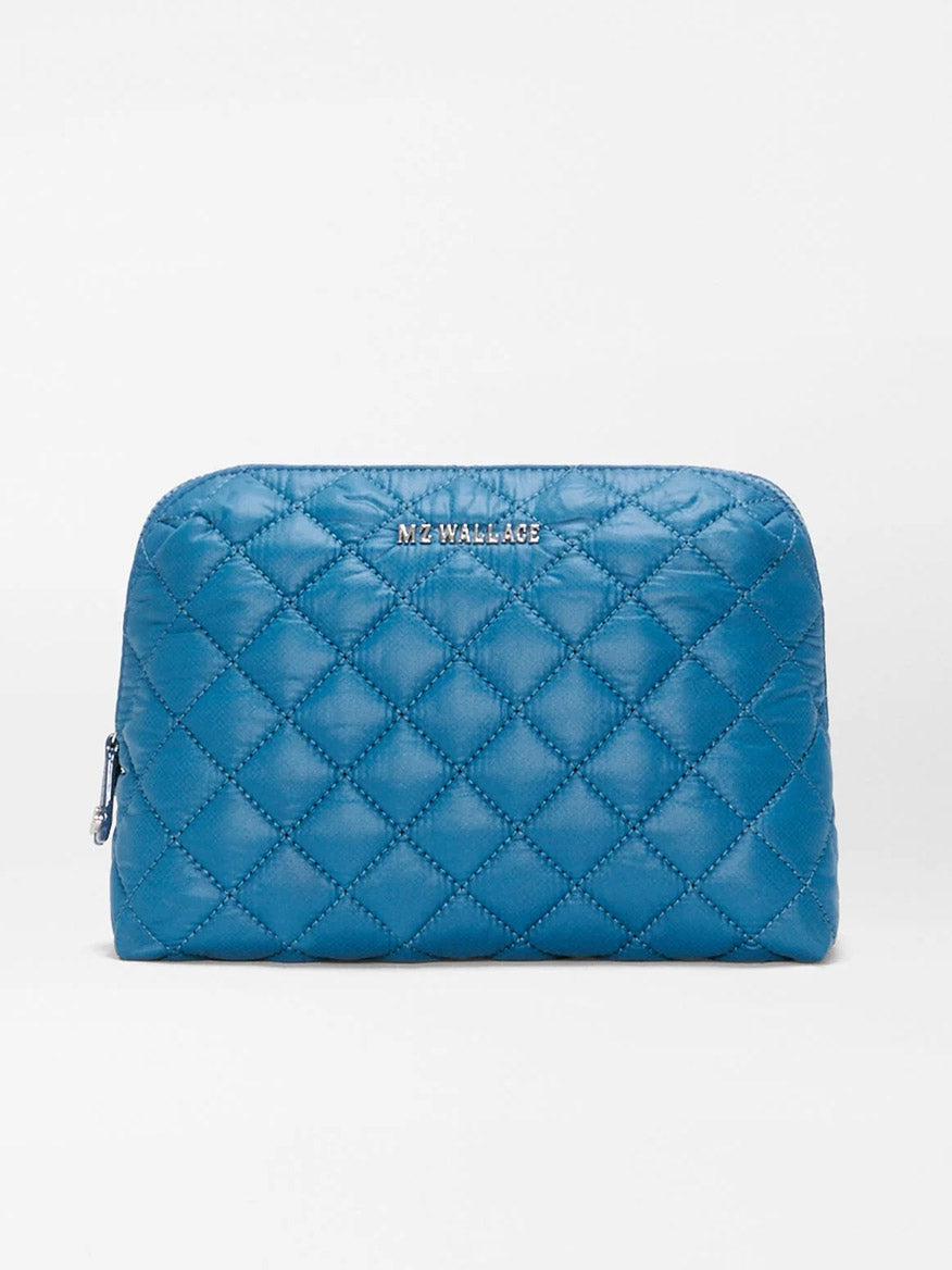 The MZ Wallace Medium Double Zip Cosmetic in Atlantic Blue Oxford is a quilted pouch bag made from recycled nylon, featuring zippered side openings perfect for organizing travel essentials, and is finished with the “MZ WALLACE” label on the front, displayed against a plain light background.