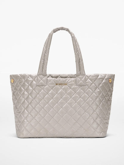 The MZ Wallace Medium East West Metro Tote in Sable Pearl Metallic Oxford features quilted silver-gray fabric, Italian leather trim, dual handles, gold-tone hardware, and a subtle front logo—stylish and ideal as a laptop bag.