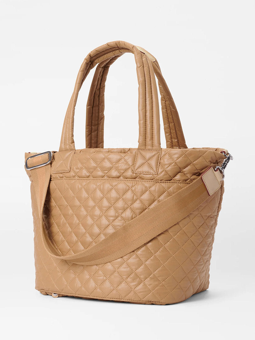 The MZ Wallace Medium Metro Tote Deluxe in Caramel Oxford, made of a tan quilted design with Italian leather trim, includes two handles and an adjustable shoulder strap, elegantly set against a minimalist background.