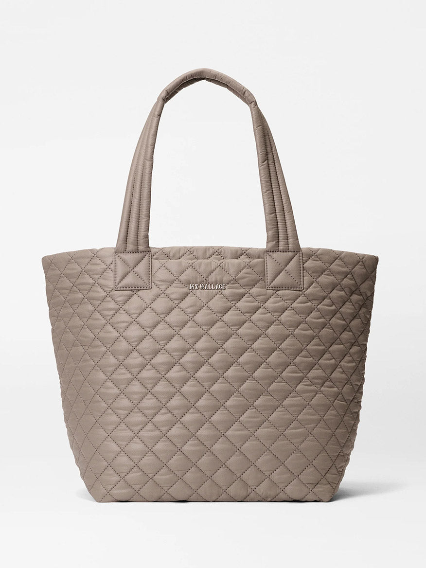 The MZ Wallace Medium Metro Tote Deluxe in Morning Dove Oxford, featuring quilted taupe fabric, diamond stitching, dual handles, an adjustable crossbody strap, and a subtle metallic front logo, is shown on a plain white background.
